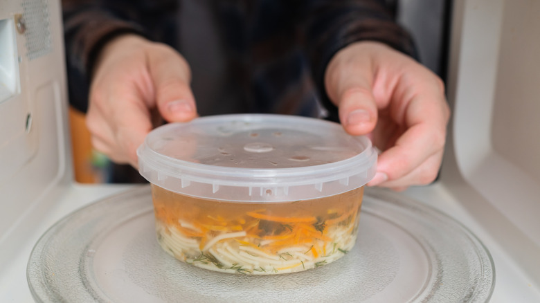 Hands placing a plastic container of soup into a microwave
