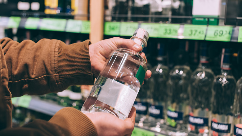 Hands holding up a bottle of clear liquor in a liquor store