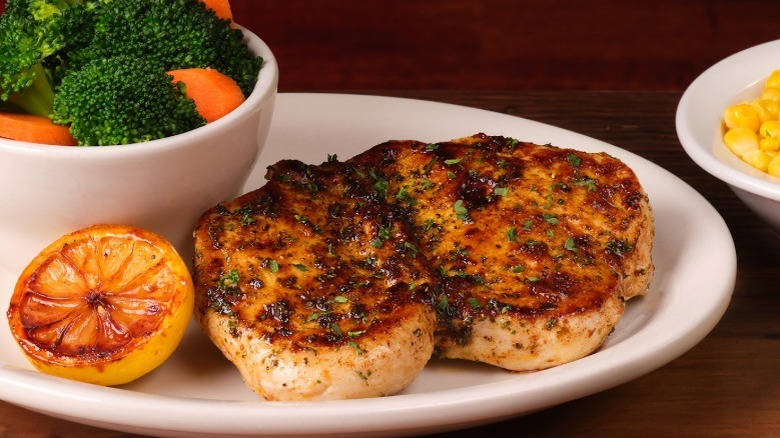 Texas Roadhouse herb-crusted chicken on a plate with half a lemon and a bowl of carrots and broccoli