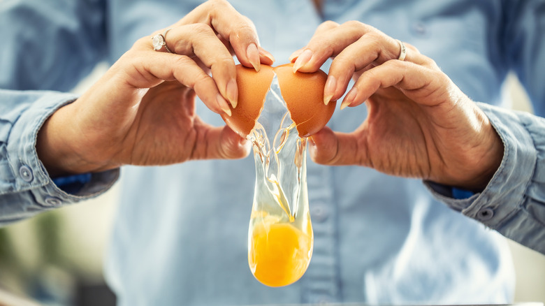 Someone cracking an egg with both hands, with the egg contents falling to bottom of frame