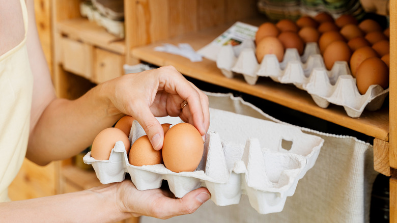 Someone standing at a pantry, holding an egg carton and lifting one egg out to inspect