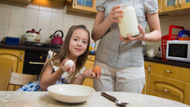 A young girl in a kitchen, holding a white egg and a brown egg