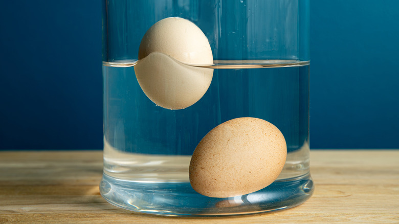 Two eggs in water, one floating and one lying on the bottom of the glass