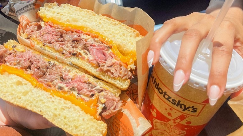 hands holding a Schlotzsky's drink and sandwich in a car