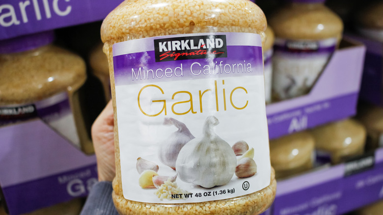 Shopper's hand holding a large jar of Kirkland Signature minced garlic