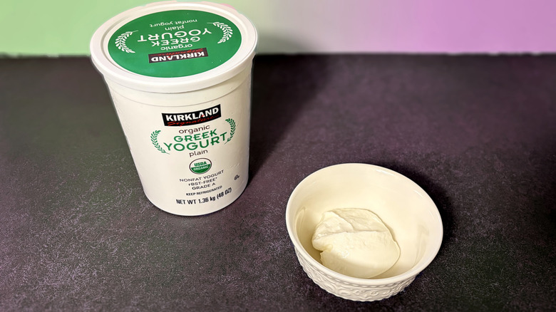 A tub of Kirkland Signature Greek yogurt and a scoop in a white bowl