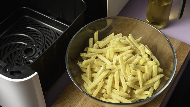 A bowl of frozen French fries next to an air fryer basket