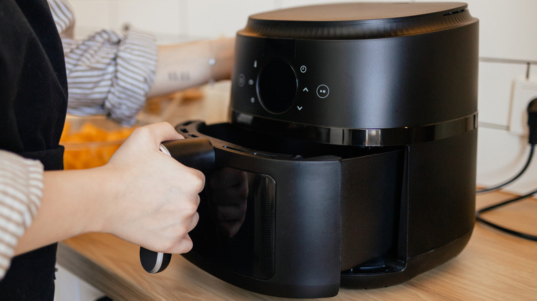 A person putting an air fryer basket in place
