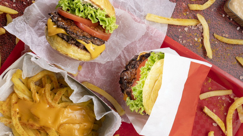 A fast food spread of two double cheeseburgers with lettuce and tomato, and seasoned cheese fries
