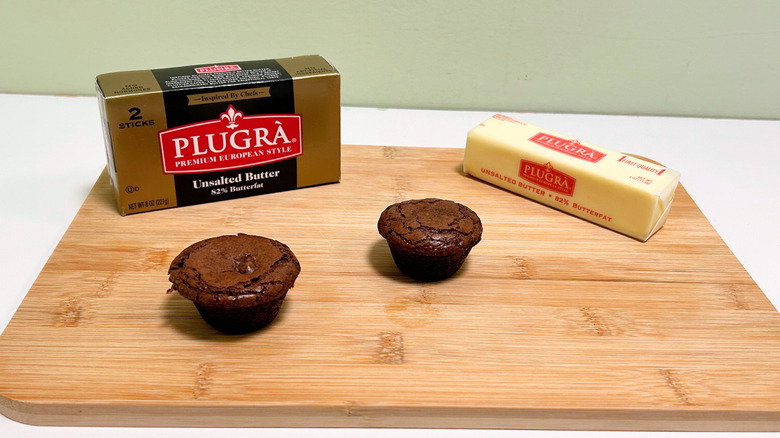 A box of Plugra Premium European Style Unsalted Butter next to a stick of butter and two brownie bites