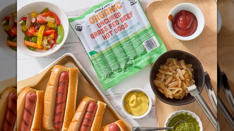 Trader Joe's Organic Uncured Grass-Fed Beef Hot Dogs on a table, surrounded by hot dogs and toppings