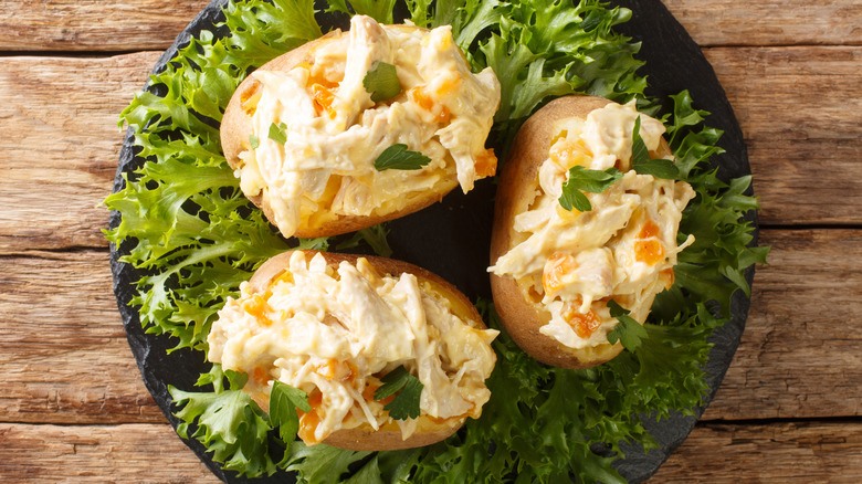 Coronation chicken baked potatoes on a bed of greens on a black plate