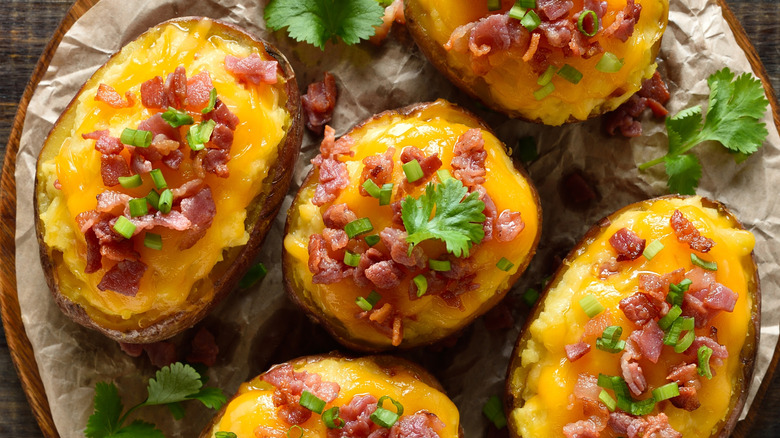 Overhead view of baked potatoes with cheese, bacon, and herb garnishes