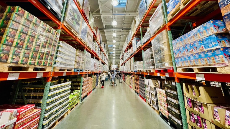 shoppers in a costco aisle with shelves packed with bulk items