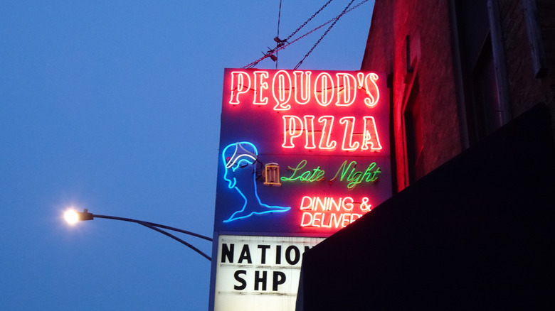 The exterior of Pequod's Pizza showing a neon sign with the restaurant name plus "Late Night Dining & Delivery"