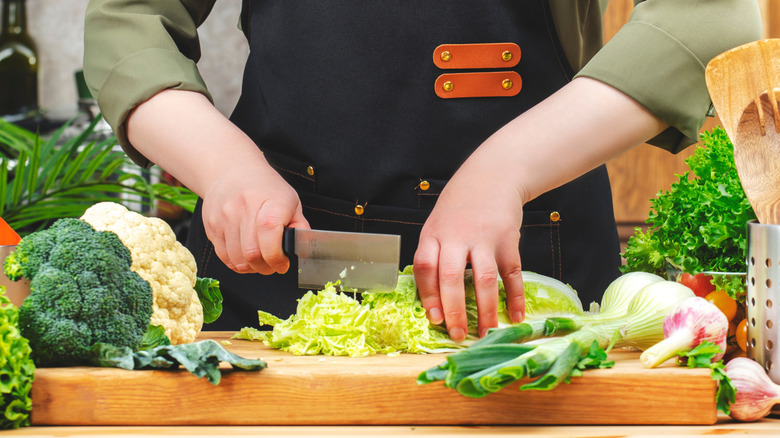 Chef cutting cabbage with nakiri knife with other veggies around
