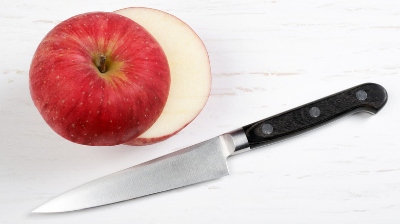 Petty knife with black handle next to halved apple