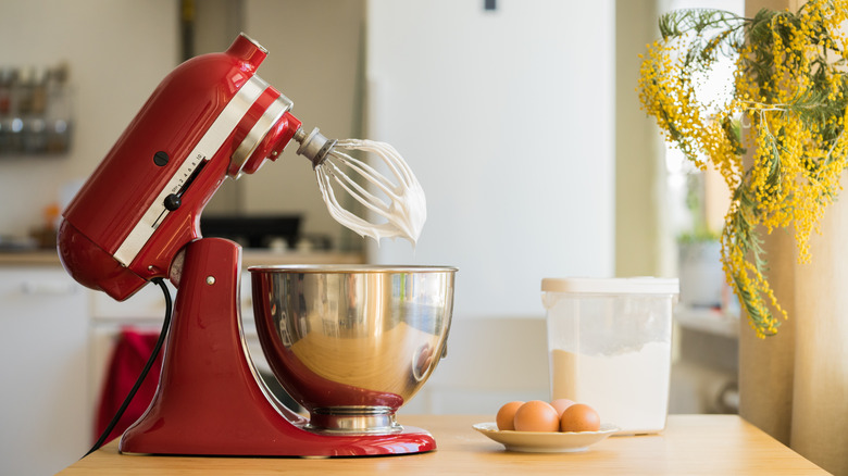 A red stand mixer tilted up with a beater covered in whipped cream