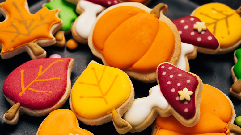 An assortment of fall-themed iced sugar cookies. The pumpkin cookies have well-defined gourd ridges