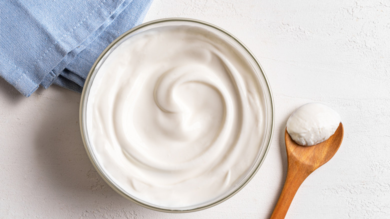 Bowl of sour cream and wooden spoon with sour cream.