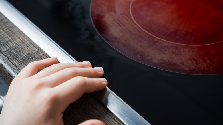 A child's hand reaches towards an electric burner that is on