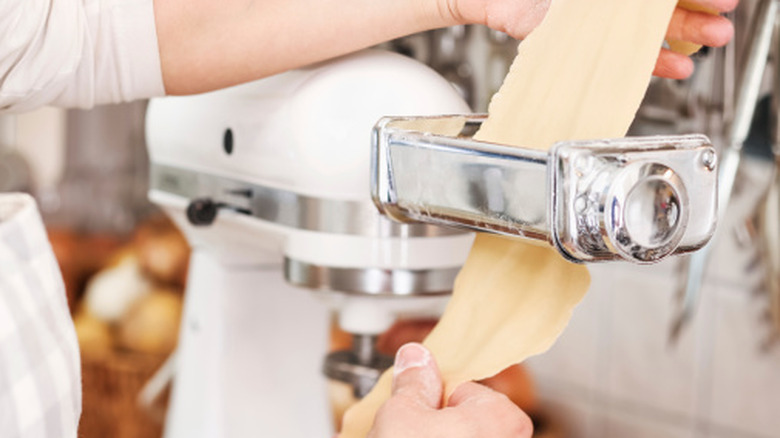 A baker rolls pasta dough through a stand mixer pasta attachment