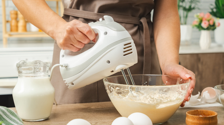 Woman using a handheld mixer to mix batter while holding the bowl