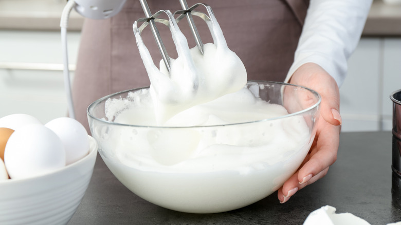 A woman in an apron whips egg whites with a hand mixer
