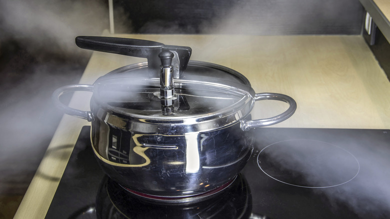 A silver-colored pressure cooker venting steam in an X-shape on an electric range