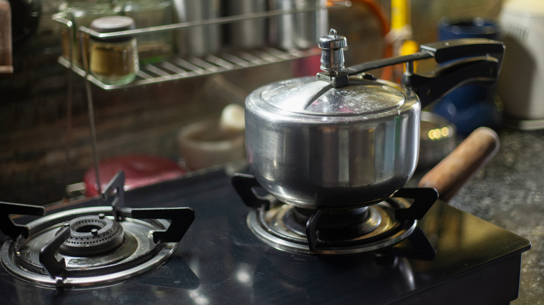 A silver-colored pressure cooker on a small gas cooktop