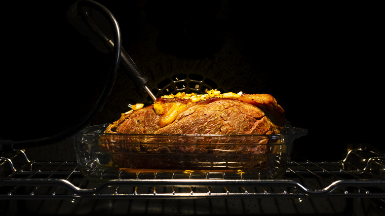 A glass dish filled with roast meat on an oven rack