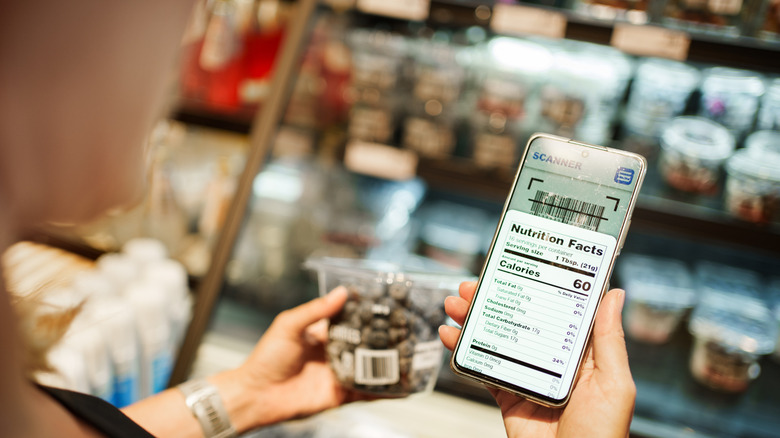 Woman holds up a food item alongside the nutrition facts for the item on her phone
