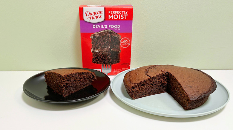 A box of Duncan Hines Perfectly Moist Devil's Food Cake Mix next to two plates of cake