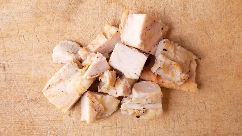 Cubes of roasted chicken on wooden cutting board