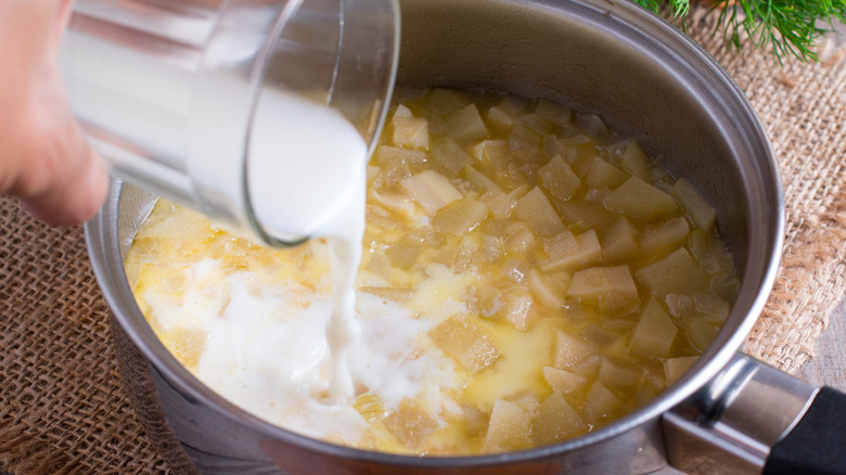 Pouring glass of milk into pot of soup