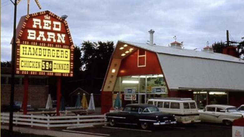 Exterior of a Red Barn location showing a parking lot and a sign advertising hamburgers and chicken dinners