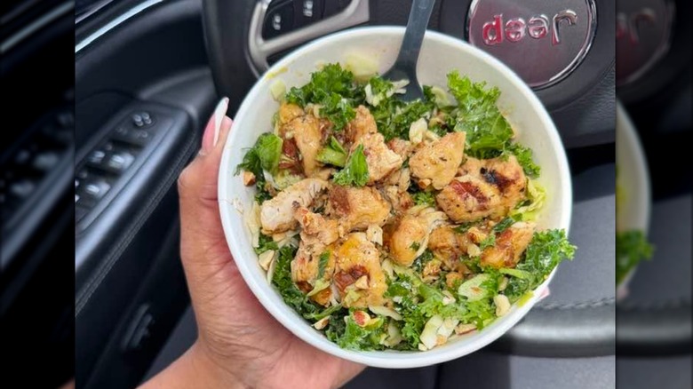 Hand holding bowl of kale salad with grilled nuggets and fork