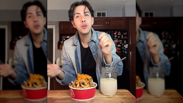 Man with bowl of chicken and jar beverage in front of him