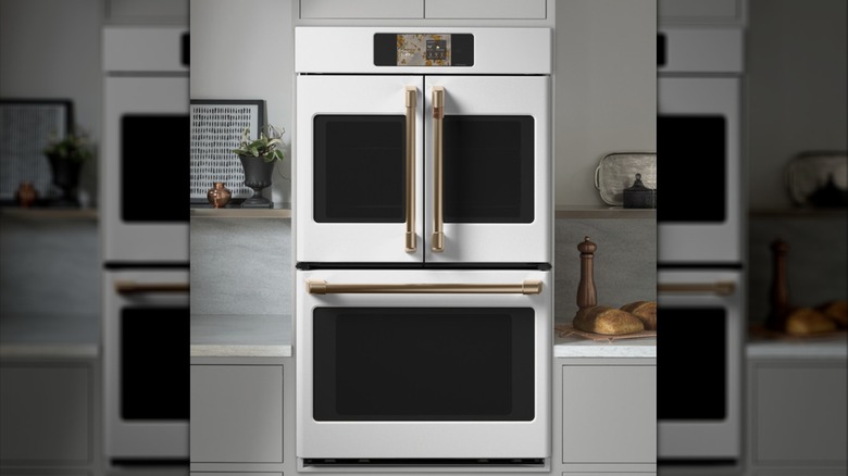 A matte white GE Café double wall oven with French doors and polished brass handles