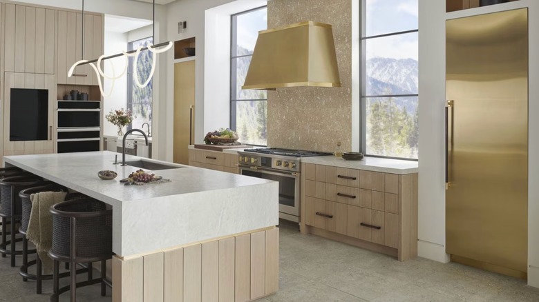 A modern kitchen with polished brass Monogram refrigerators and oven hood, and a stainless Monogram range/oven with brass accents