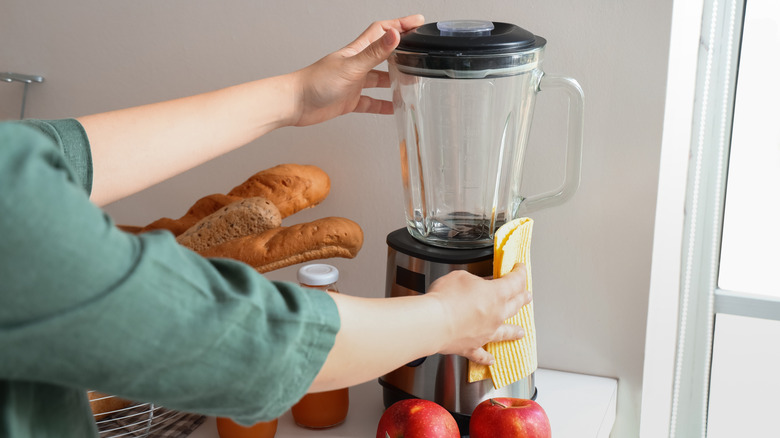 Two hands reaching forward to clean a blender with a yellow cloth