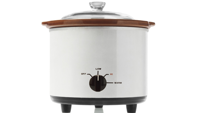 A white slow cooker with a brown top and glass lid on a white background