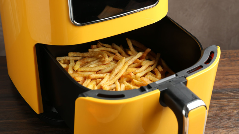 A yellow air fryer with french fries in its basket
