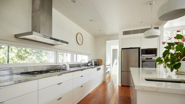 A minimalist home kitchen with white cabinets and kitchen island, and stainless steel countertops and appliances