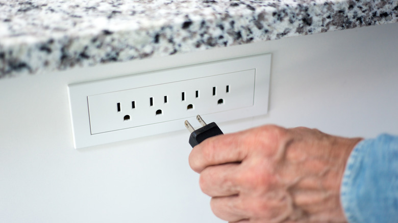 A hand plugging a black power cord into an outlet on a white kitchen island