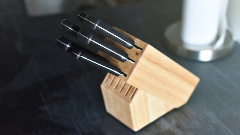 Black-handled kitchen knives in a yellow wood knife block on a dark colored countertop.
