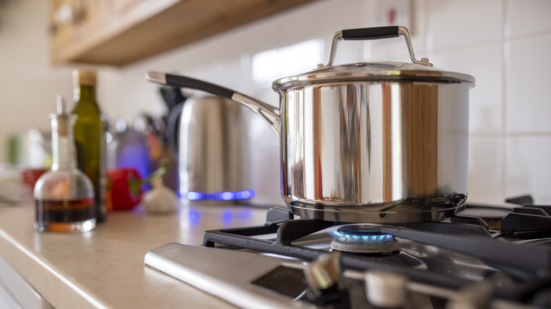 A shiny metal pot on a lit gas burner, with the handle turned over the stove