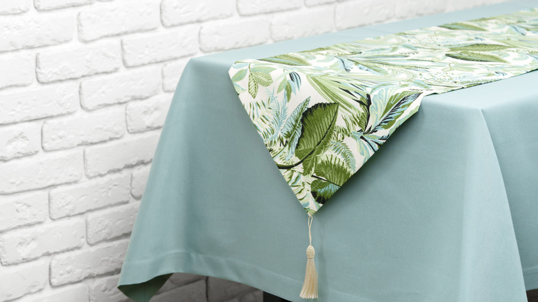 A green floral table runner on top of a table covered in a blue tablecloth