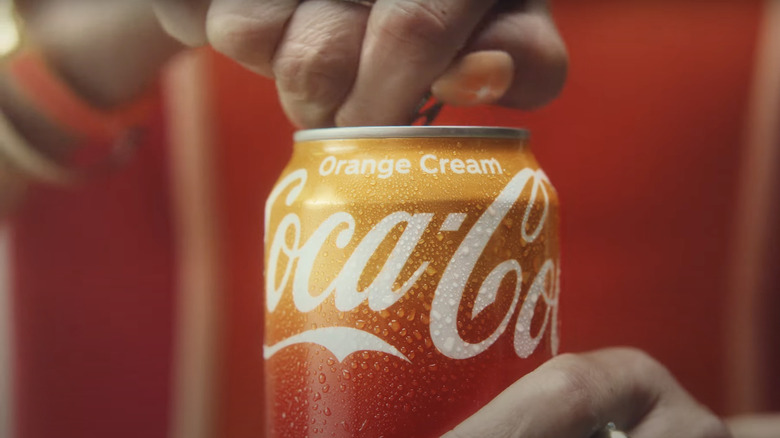 A hand opening a can of Coca-Cola Orange Cream