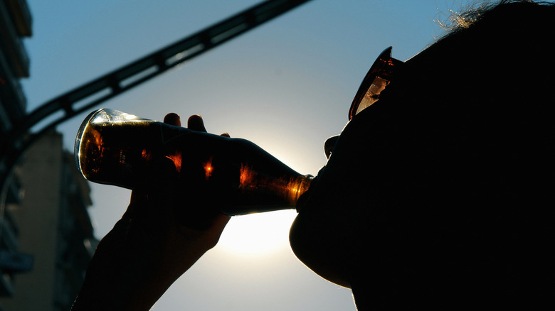Silhouette of someone drinking a glass bottle of soda